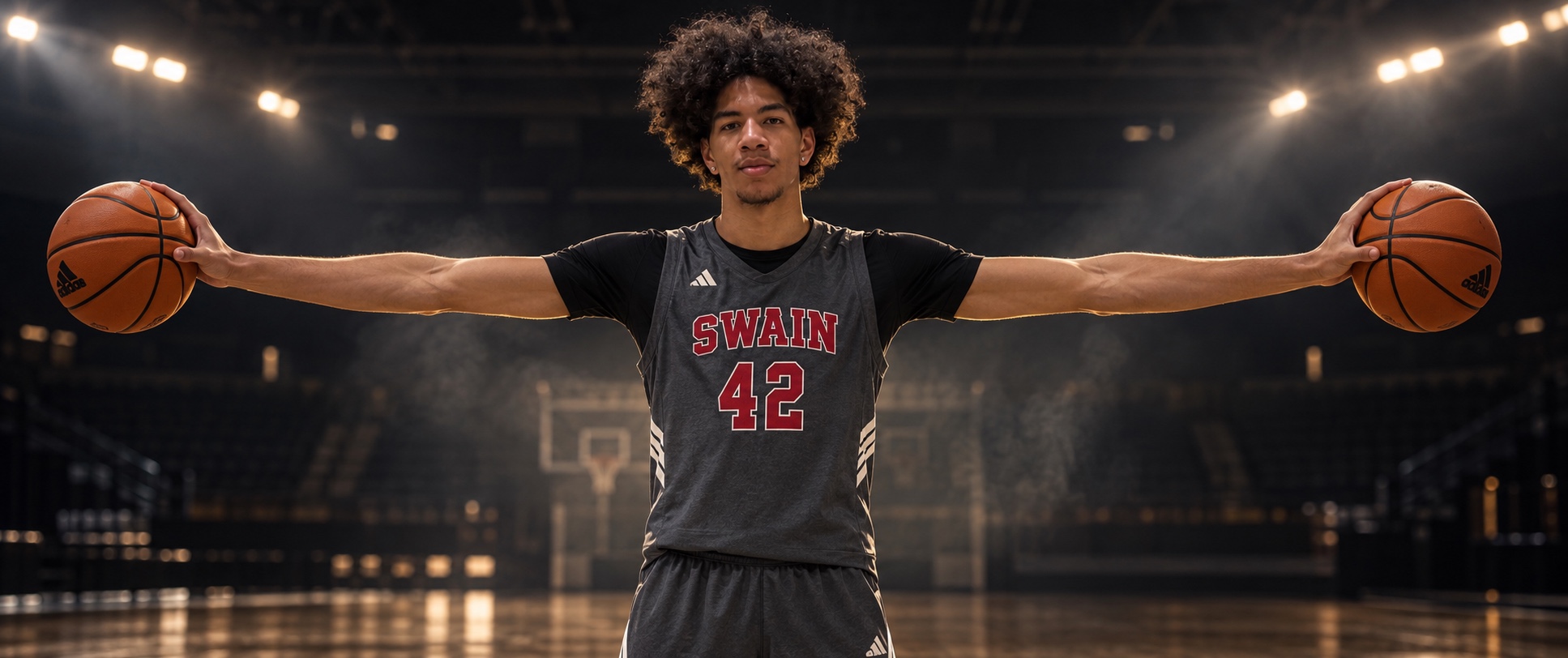 Dariel Gomez with arms extended, holding a basketball in each hand in a dark arena
